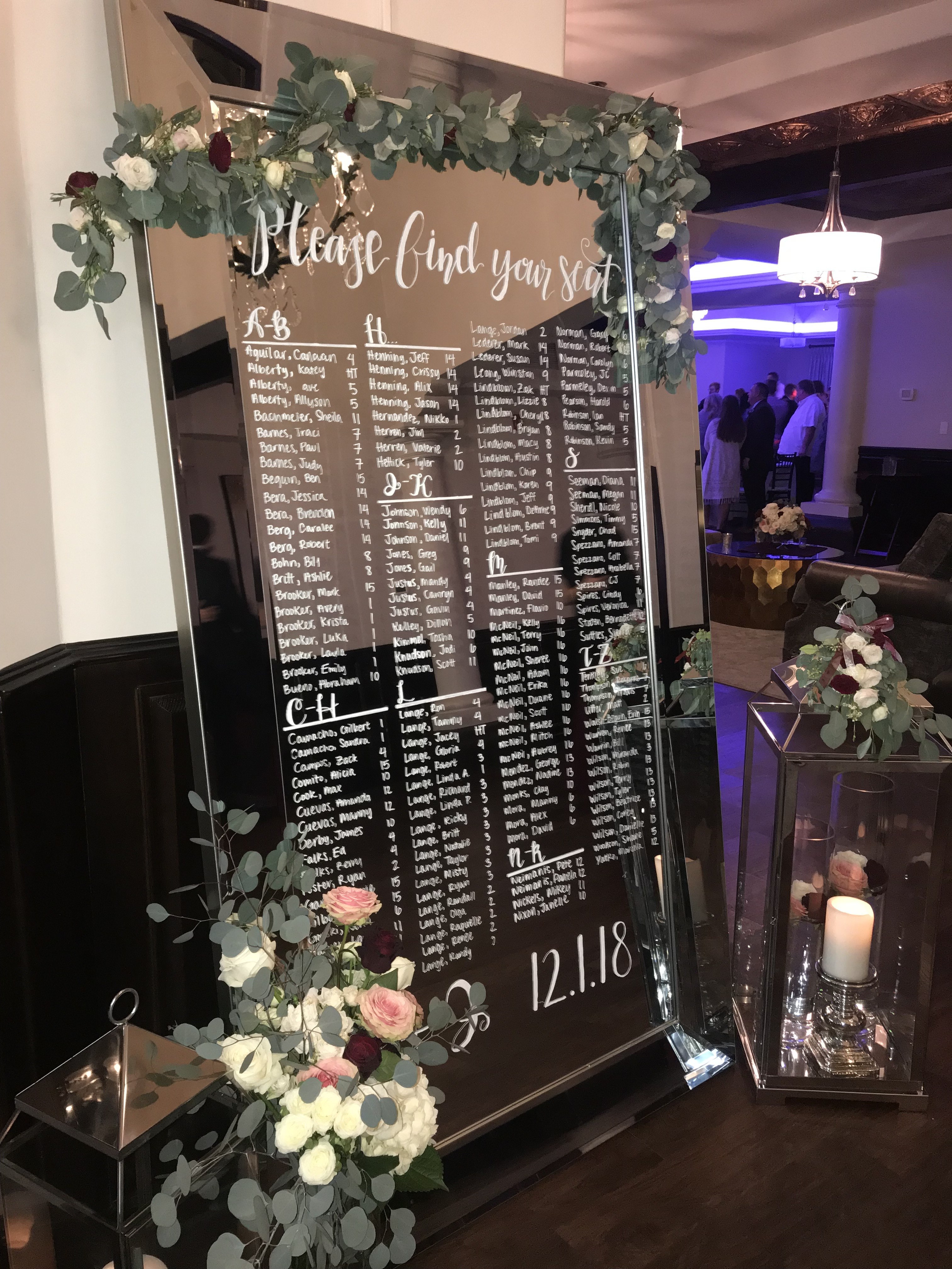 Wedding seating chart hand-lettered on a mirror with eucalyptus garland